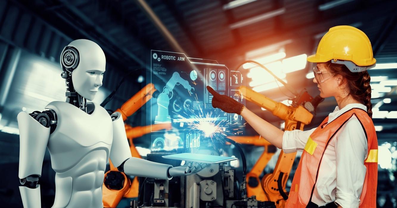 Uma mulher de capacete e óculos de segurança interage com um robô humanóide e um painel de controle holográfico em uma fábrica futurista. Braços robóticos industriais são visíveis ao fundo.