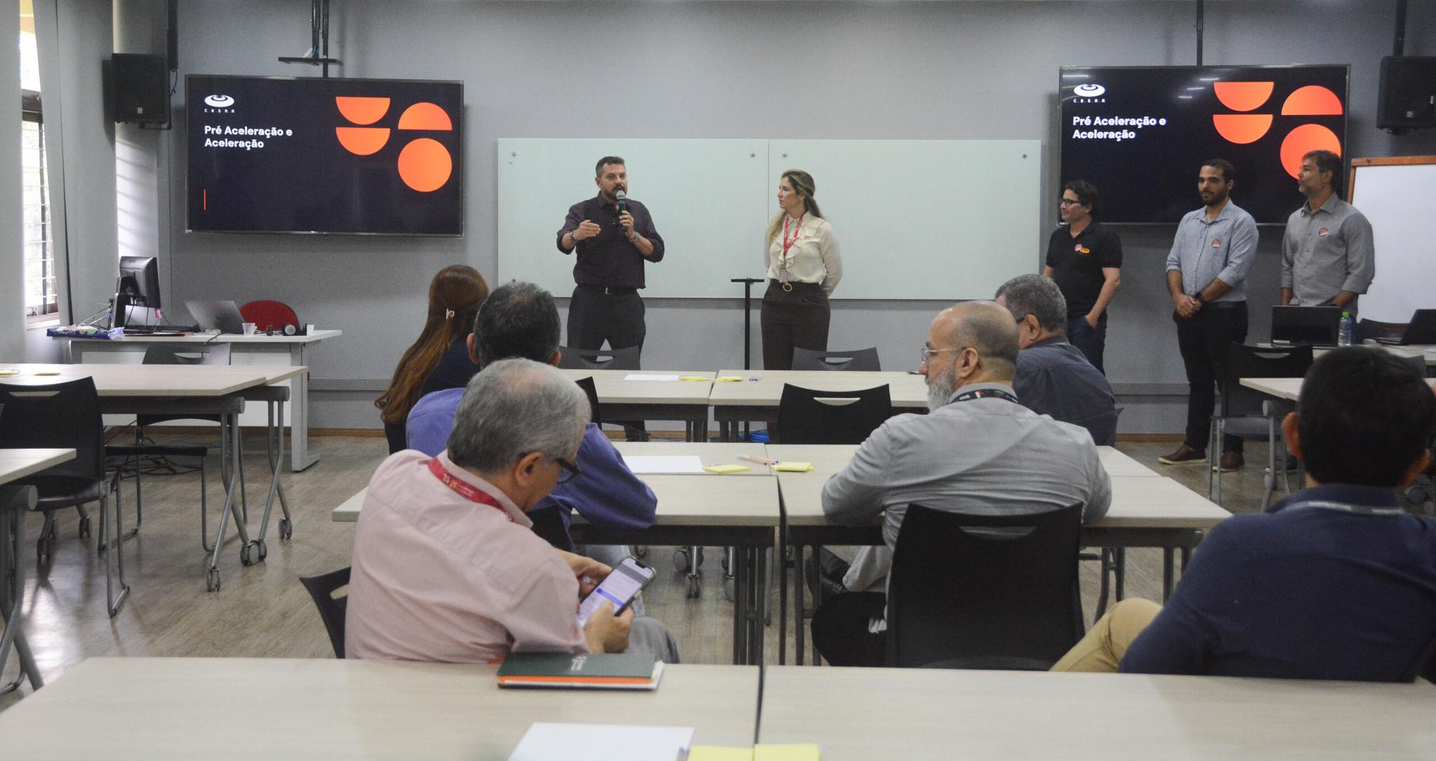 Uma pessoas palestrando em uma sala com algumas pessoas