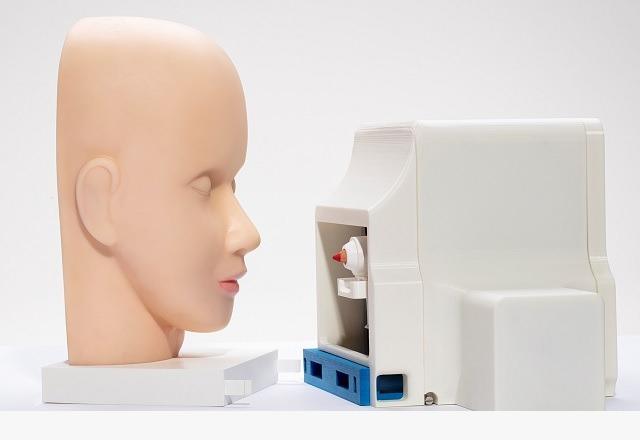 Cabeça de manequim de treinamento de maquiagem posicionada diante de um dispositivo pequeno e branco com uma pequena ferramenta dentro.