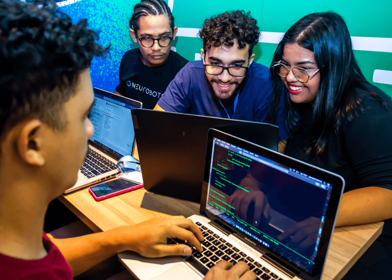 Alunos utilizando notebooks em mesa de espaço comum