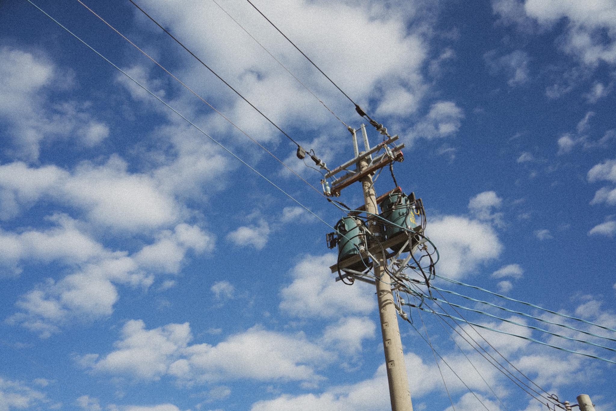 Um poste de eletricidade com transformadores e fios contra um céu azul e nublado.