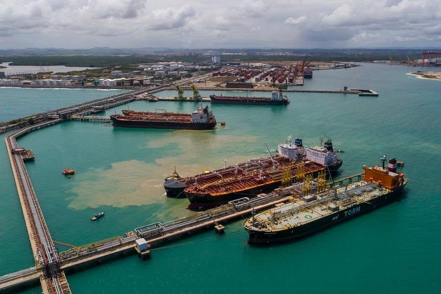 Vista aérea de petroleiros atracados em terminal portuário, mostrando infraestrutura de logística e transporte de petróleo e gás. Ensino tecnológico, engenharia, logística portuária.