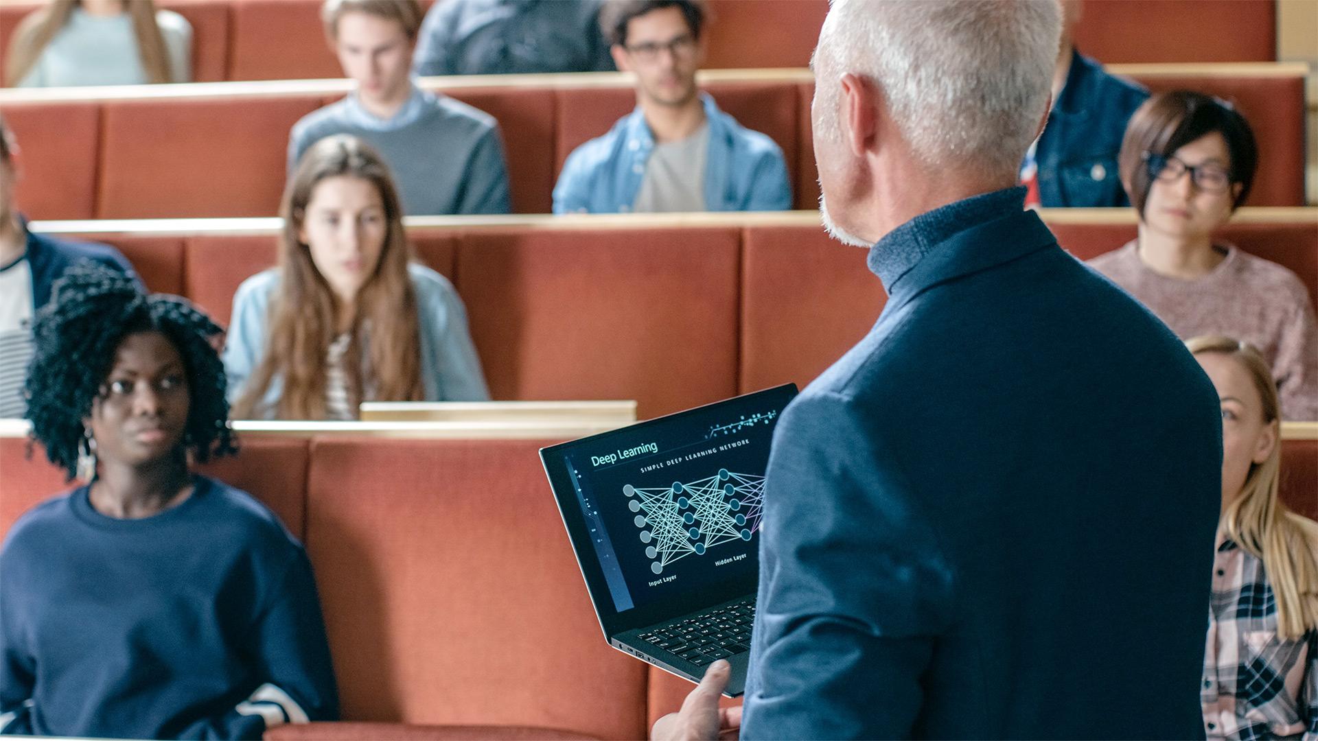 Professor apresentando aprendizado profundo em uma palestra para uma classe de estudantes universitários sentados em carteiras de auditório.