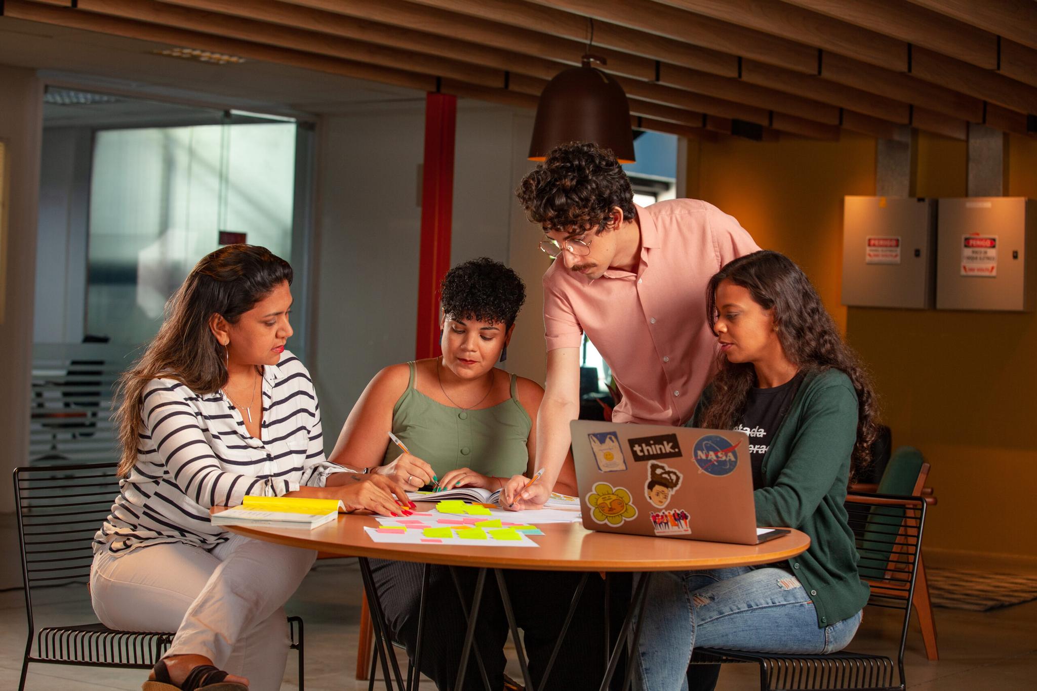 Quatro pessoas reunidas em uma mesa conversando com um notebook e realizando algumas anotações