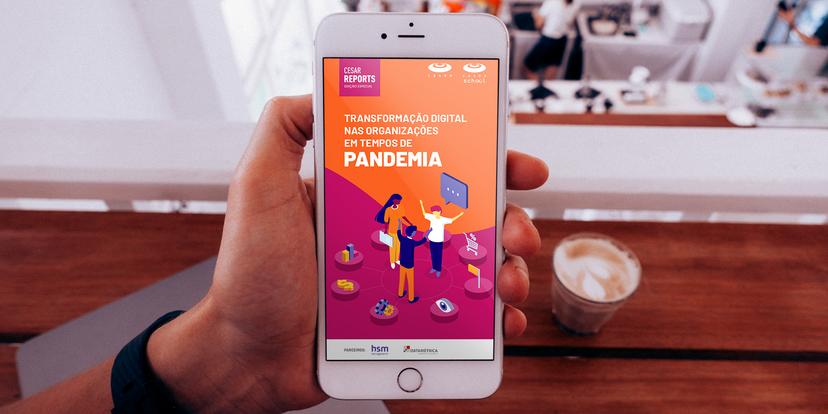 Close-up of a hand holding a smartphone displaying a report titled "Transformação Digital nas Organizações em Tempos de Pandemia".  The report features isometric illustrations of people collaborating.