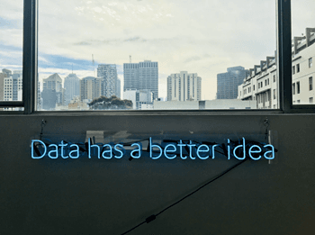 Placa de néon azul com a frase "Data has a better idea" em uma parede de escritório com vista para uma cidade.