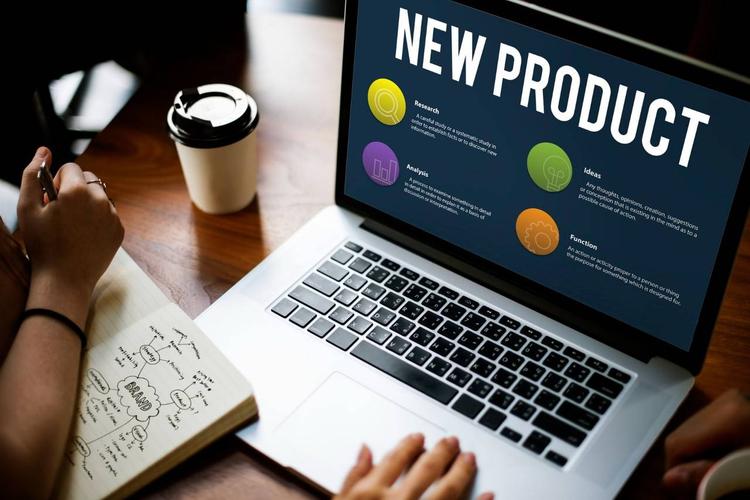 Laptop displaying "New Product" with sections on research, analysis, ideas, and function; a person takes notes nearby.