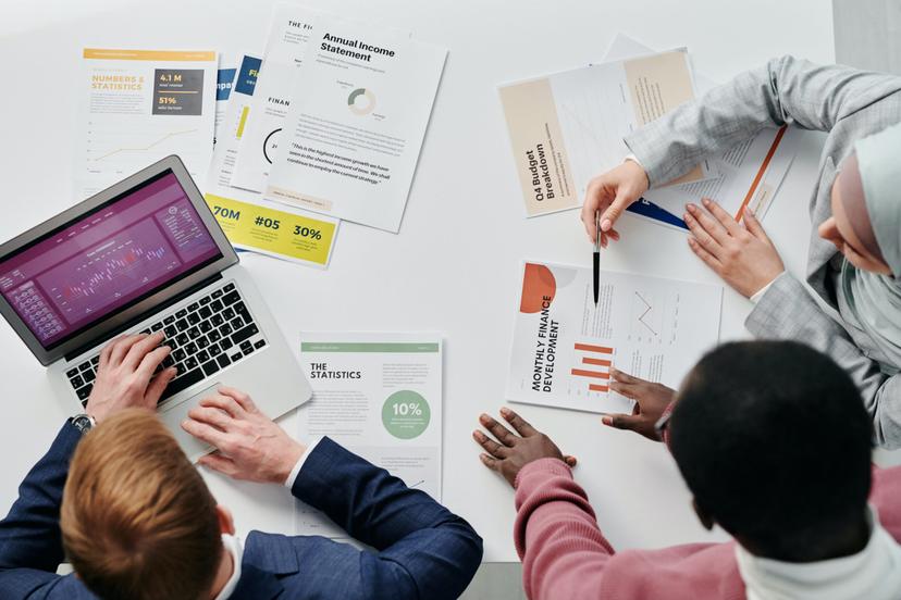 Vista aérea de três colegas analisando relatórios financeiros e gráficos em uma mesa de escritório.