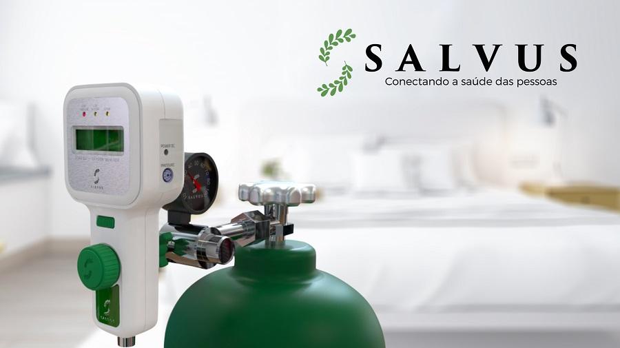 Dispositivo médico branco conectado a um cilindro de oxigênio verde, com visor digital e mostrador de pressão.  Fundo desfocado de um quarto de hospital.