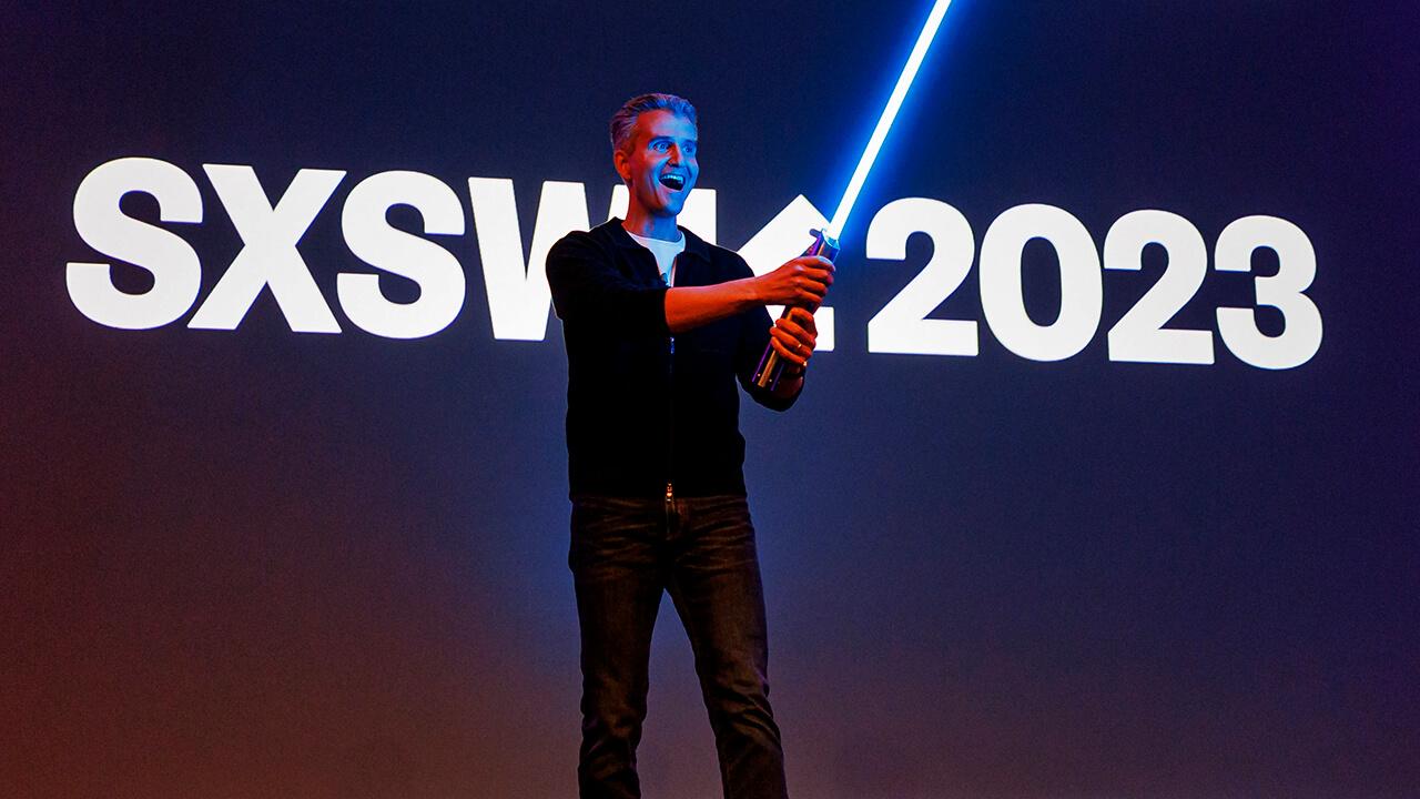 Homem com um sabre de luz na frente de um banner escrito: sxswk2023