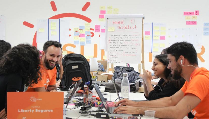 Programa Summer Job do CESAR conecta talentos e inovação aberta Jovens em volta de mesa com notebooks e post-its ao fundo. Também há uma placa que identifica turma Liberty Seguros no Summer Job