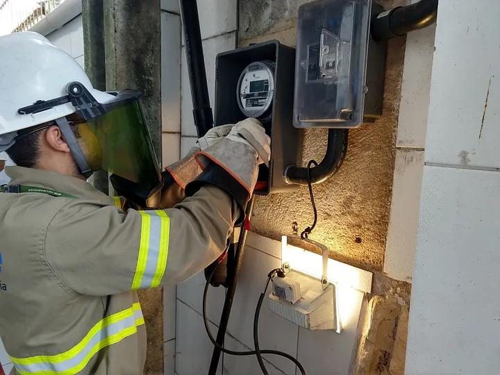 Design e inovação no sistema elétrico Eletricista com capacete e luvas instala medidor em caixa elétrica na parede, aplicando design e inovação no sistema elétrico