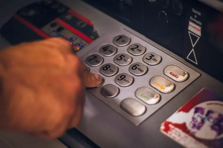 Pix e Open Banking impulsionando negócios e inovação financeira Mão pressiona os botões numéricos de metal de um caixa eletrônico bancário, com foco próximo no teclado