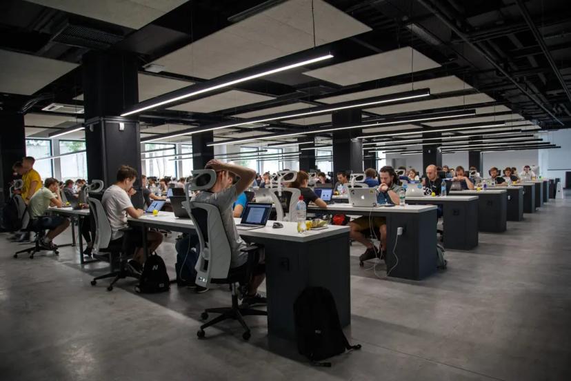 Residência de software e alternativas inteligentes para contratação em tecnologia Muitas pessoas trabalham com notebooks em várias fileiras de mesas em um grande escritório compartilhado
