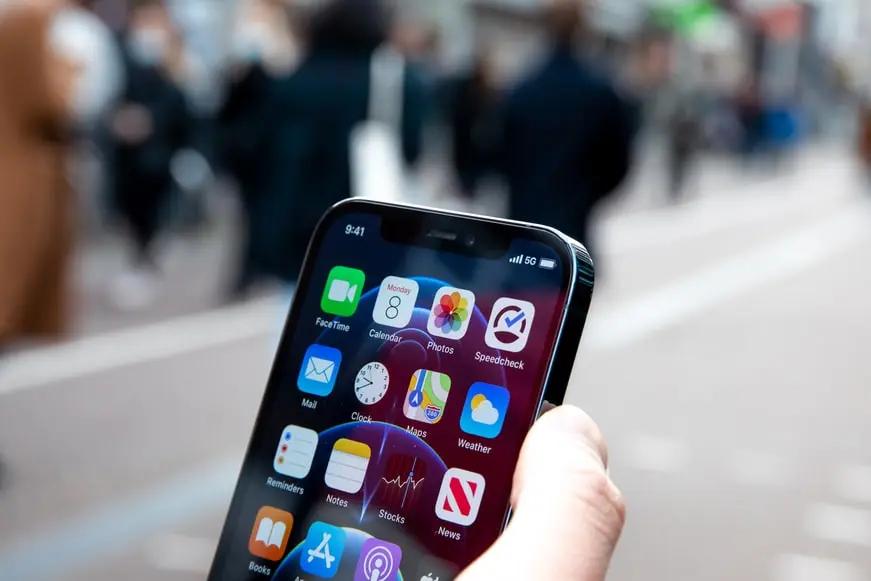 O 5G impulsionando os pilares ESG Mão segura um smartphone em primeiro plano mostrando o ícone de conexão 5G na tela, com uma rua movimentada e desfocada ao fundo