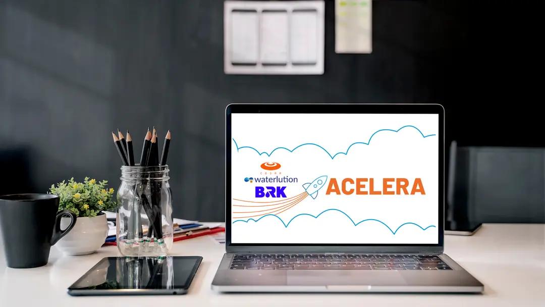 Inovação e Estratégia Empresarial no Programa Acelera da BRK e CESAR Notebook aberto em mesa de escritório exibe o logo Acelera com ícone de foguete, marcas BRK, Waterlution e CESAR ao fundo.