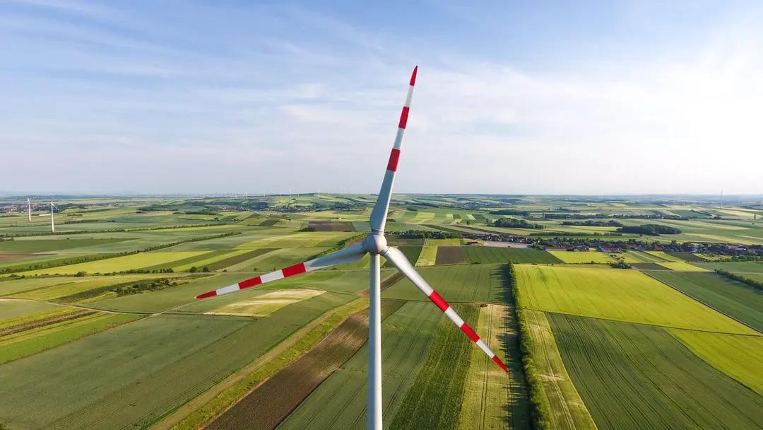 Energias renováveis no Brasil e o cenário atual de investimentos no setor Grande turbina eólica com pontas das pás pintadas de vermelho destaca-se em campo aberto verde sob céu claro e ensolarado.