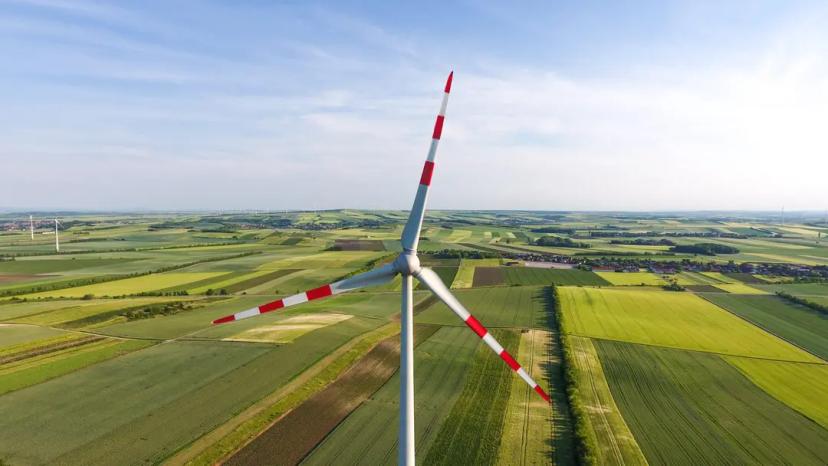 Energias renováveis no Brasil e o cenário atual de investimentos no setor Grande turbina eólica com pontas das pás pintadas de vermelho destaca-se em campo aberto verde sob céu claro e ensolarado.