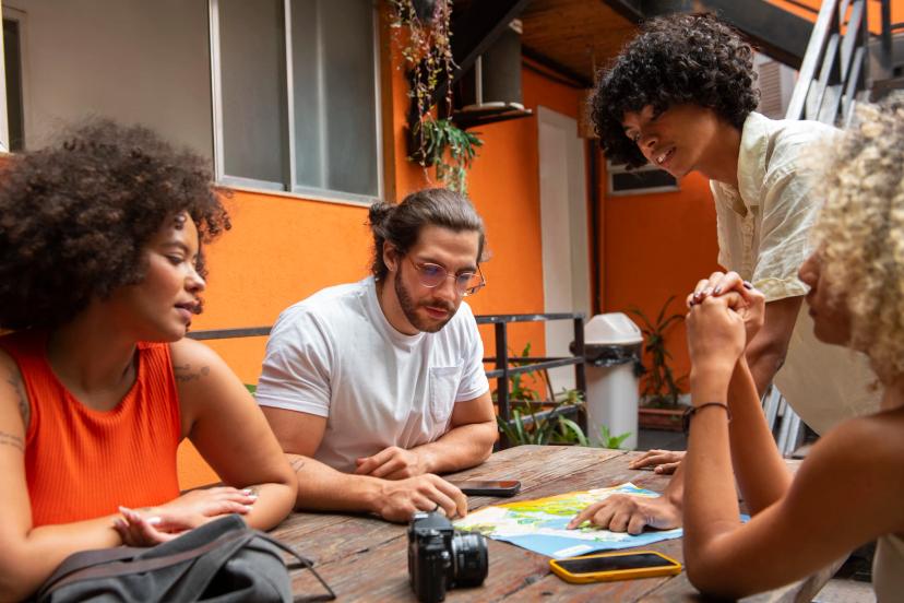 Bettcamp – Soluções Inovadoras para Educação e Inovação no CESAR Quatro pessoas reunidas ao redor de mesa analisando mapa em ambiente colaborativo de inovação na educação
