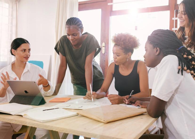 Cultura Design Driven em Projetos de Inovação Cinco mulheres em reunião colaborativa ao redor de uma mesa com tablet e cadernos, discutindo um projeto de design estratégico.