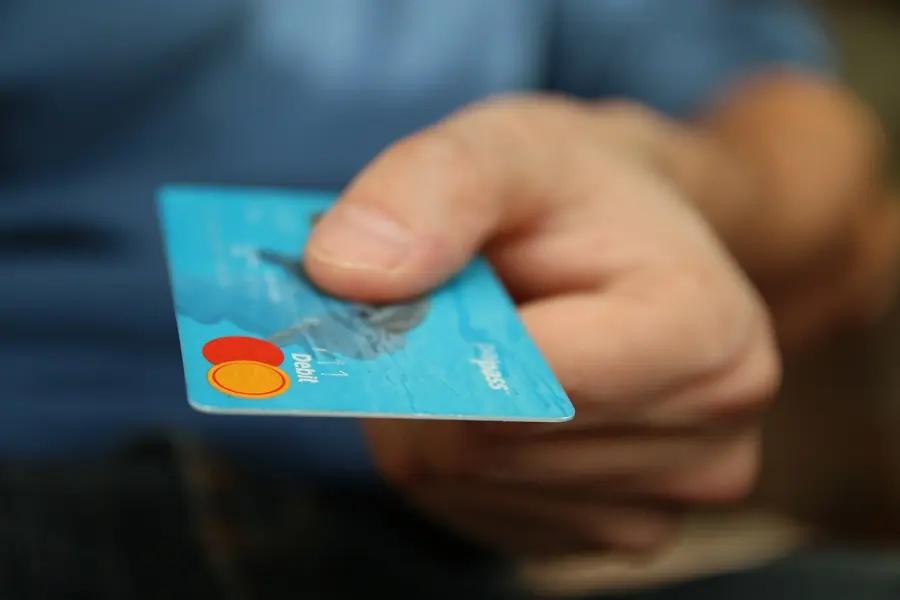 Pagamento com cartão e a evolução das fintechs no setor financeiro Mão masculina em close segurando cartão de débito azul com símbolo de aproximação, representando pagamentos digitais em fintechs.