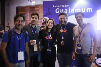 Corporate Venture Building – Acelerando Startups com allugg e CESAR Cinco profissionais sorridentes usam crachás em frente a um painel azul escrito Patrocinador Guaiamum em um evento.