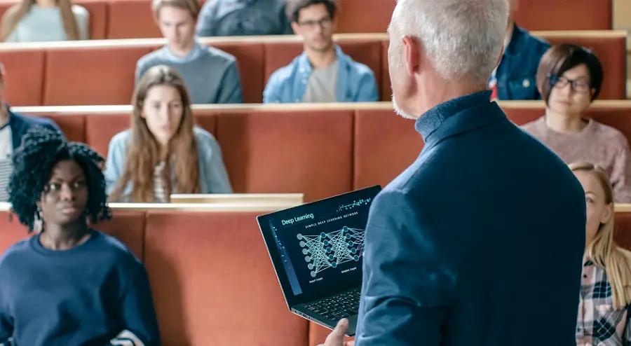 Inteligência artificial generativa na educação e o futuro da aprendizagem Professor de costas segura portátil com gráfico de Deep Learning diante de estudantes atentos num auditório universitário.