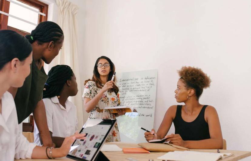 Gestão do conhecimento e por que ela é fundamental para sua empresa Cinco pessoas sorridentes em reunião de planejamento ao redor de uma mesa com notebooks e café em escritório moderno.