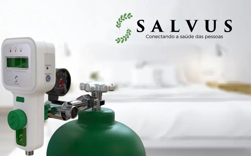 Oxigenoterapia com Salvus ATAS O2 Monitor digital Salvus acoplado a um cilindro de oxigênio verde. Logotipo Salvus ao fundo em ambiente hospitalar desfocado.