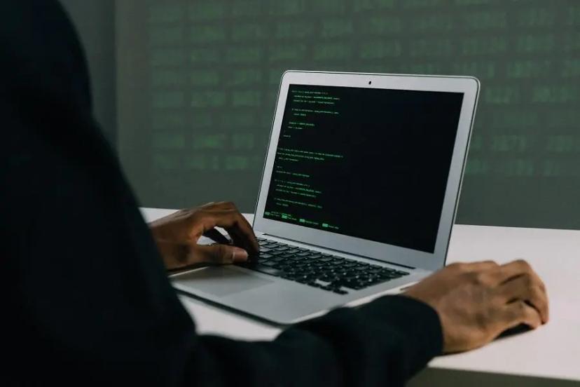 Inteligência artificial para detecção de fraudes no suporte ao cliente Mãos de uma pessoa programando em um laptop que exibe linhas de código verdes em uma tela preta, em ambiente escuro.