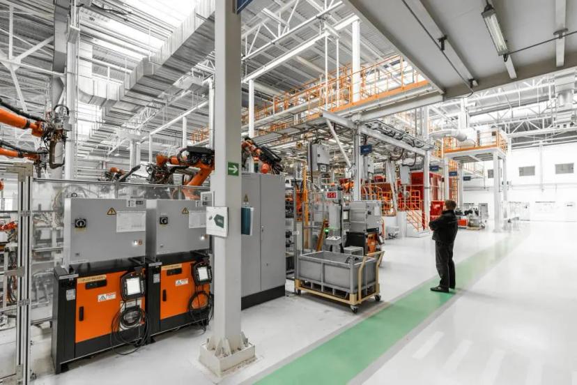 Lei de Informática de Manaus – Suframa e incentivos para a indústria Operário observa braços robóticos em uma ampla fábrica automatizada com painéis de controle laranja e estruturas metálicas.