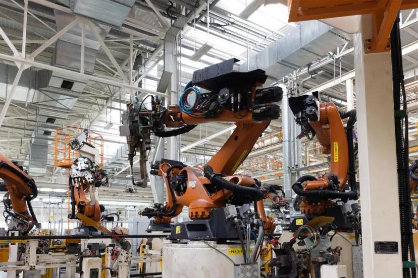 Inovação na indústria com integração e automação de processos fabris Vários braços robóticos industriais laranja em linha de montagem dentro de uma fábrica com estrutura metálica branca.