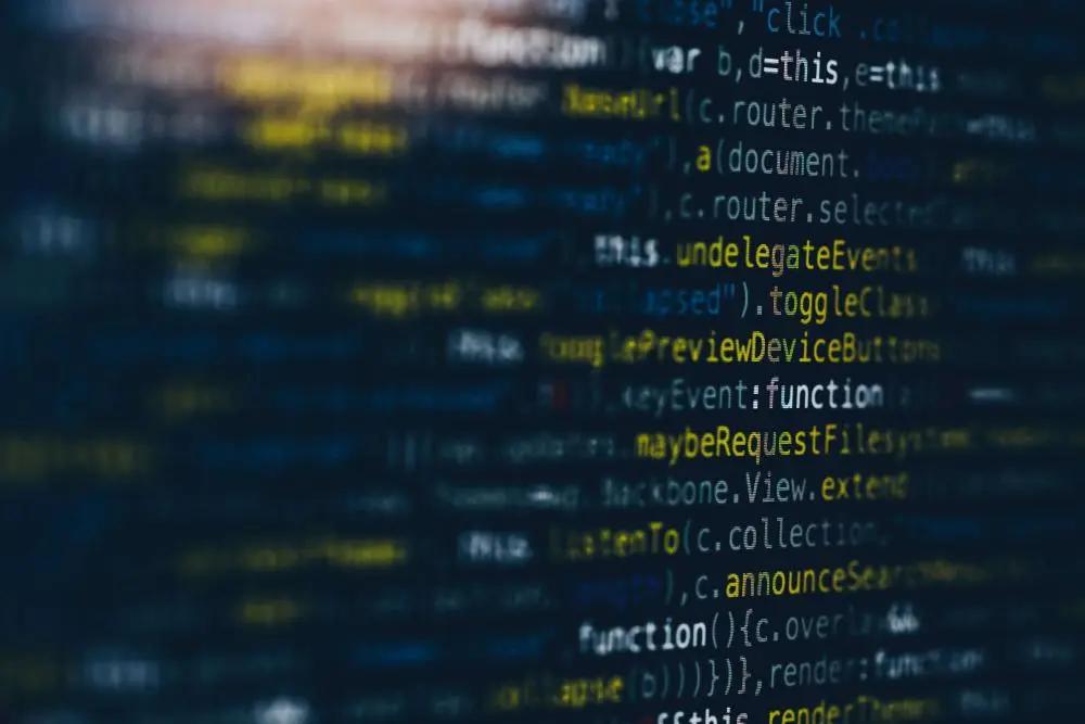 Inovação na indústria – como converter dados em novos negócios Tela de computador em close-up exibindo linhas coloridas de código de programação JavaScript em um fundo escuro desfocado.