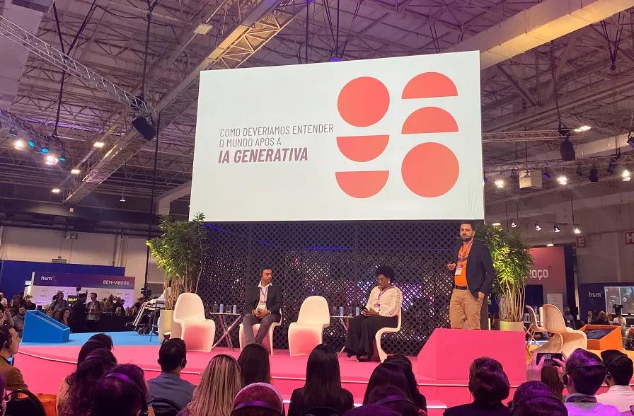 Mercado de trabalho, inteligência artificial e o futuro das profissões Palestrantes em palco rosa diante de telão com o texto "Como deveríamos entender o mundo após a IA Generativa"