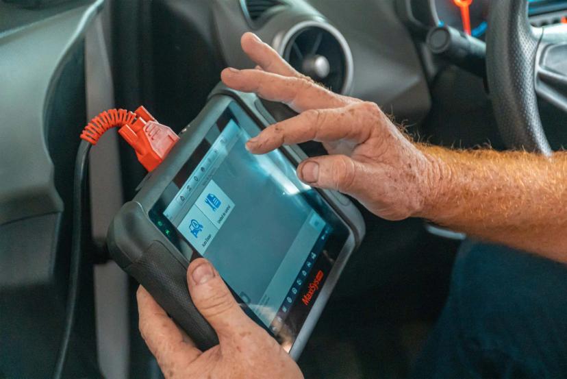 Setor de mobilidade e diagnóstico veicular com scanner digital avançado Mãos de técnico operando tablet de diagnóstico automotivo conectado por cabo laranja ao painel interno de um veículo.