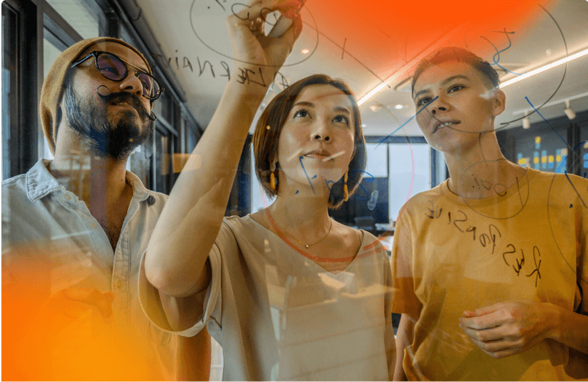 Fazemos parte de uma Rede de Inovação Aberta Três pessoas olhando e escrevendo em uma lousa transparente