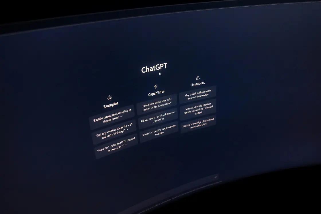 Inteligência artificial no ambiente corporativo e a interface do ChatGPT Monitor de computador exibindo a interface inicial do ChatGPT com colunas de exemplos, capacidades e limitações em fundo escuro.