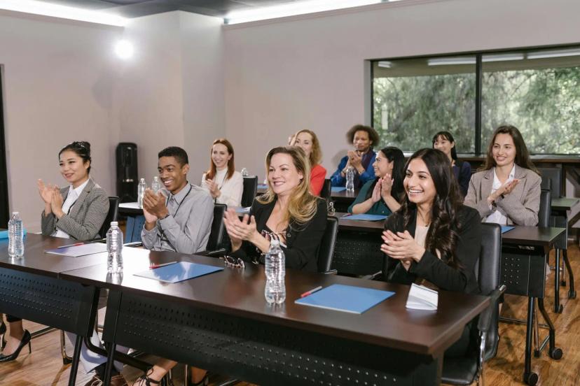Parcerias estratégicas entre empresas e instituições de pesquisa Grupo diverso de profissionais sorridentes aplaudindo em auditório durante palestra sobre cooperação e inovação tecnológica.