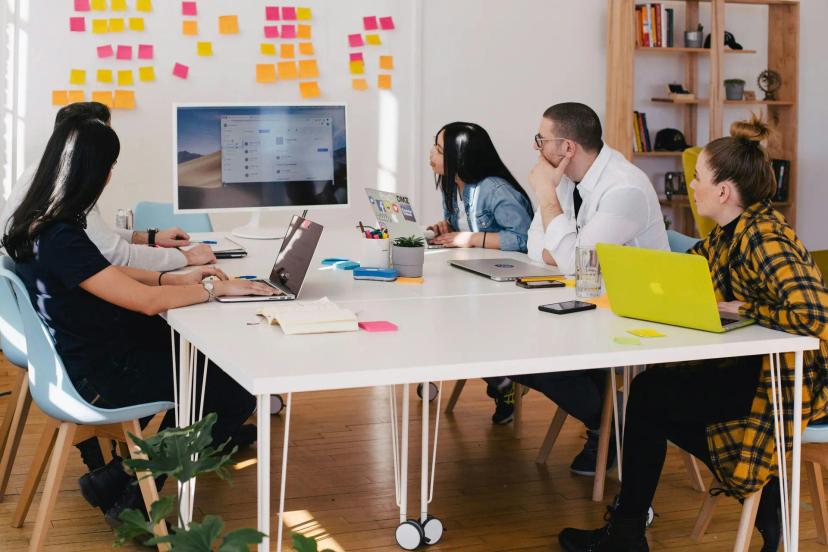 Apoio da Embrapii para Startups e PMEs Equipe de cinco pessoas em mesa branca com notebooks analisando tela; parede branca ao fundo com diversos post-its coloridos.