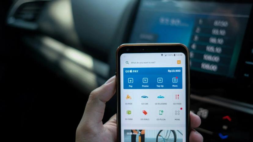 Inovação digital financeira e o uso de aplicativos bancários no dia a dia Mão segurando smartphone com aplicativo de pagamentos e serviços aberto dentro de um carro com painel digital ao fundo.