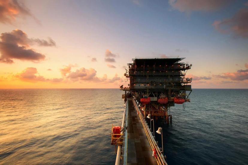 Inovações tecnológicas para eficiência energética em plataformas offshore Plataforma de petróleo offshore conectada por passarela metálica sobre o mar durante o pôr do sol sob céu alaranjado.