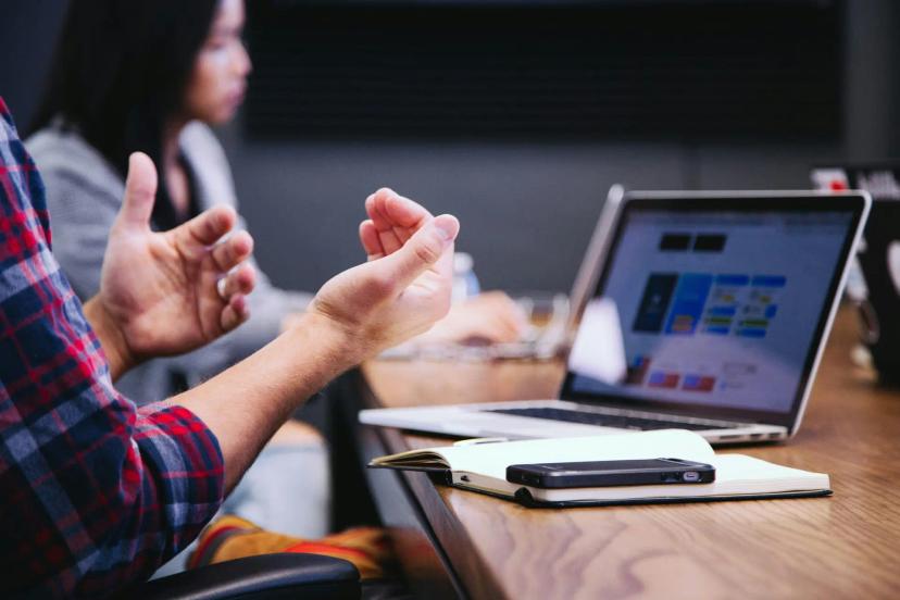 Aprendizagem digital e práticas inovadoras no ensino corporativo Duas pessoas em reunião com notebook aberto, caderno e smartphone, discutindo estratégias de aprendizagem digital.