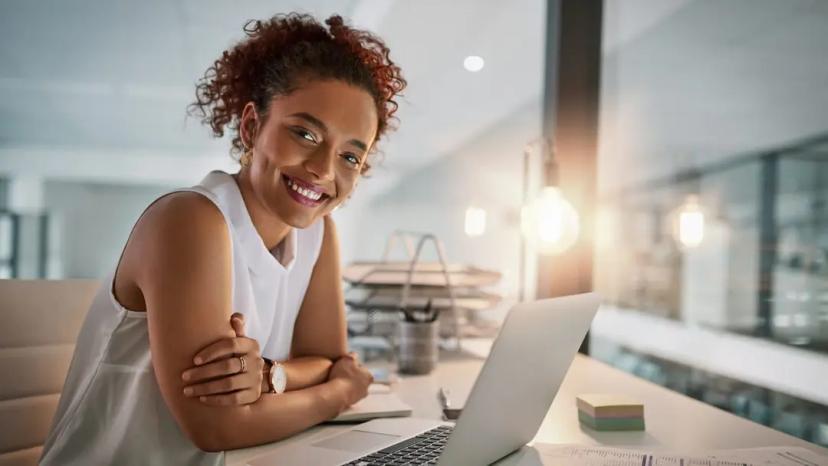 Impacto da IA na experiência do cliente no setor elétrico Profissional sorrindo usa notebook em escritório moderno, analisando dados com IA aplicada à experiência do cliente no setor elétrico