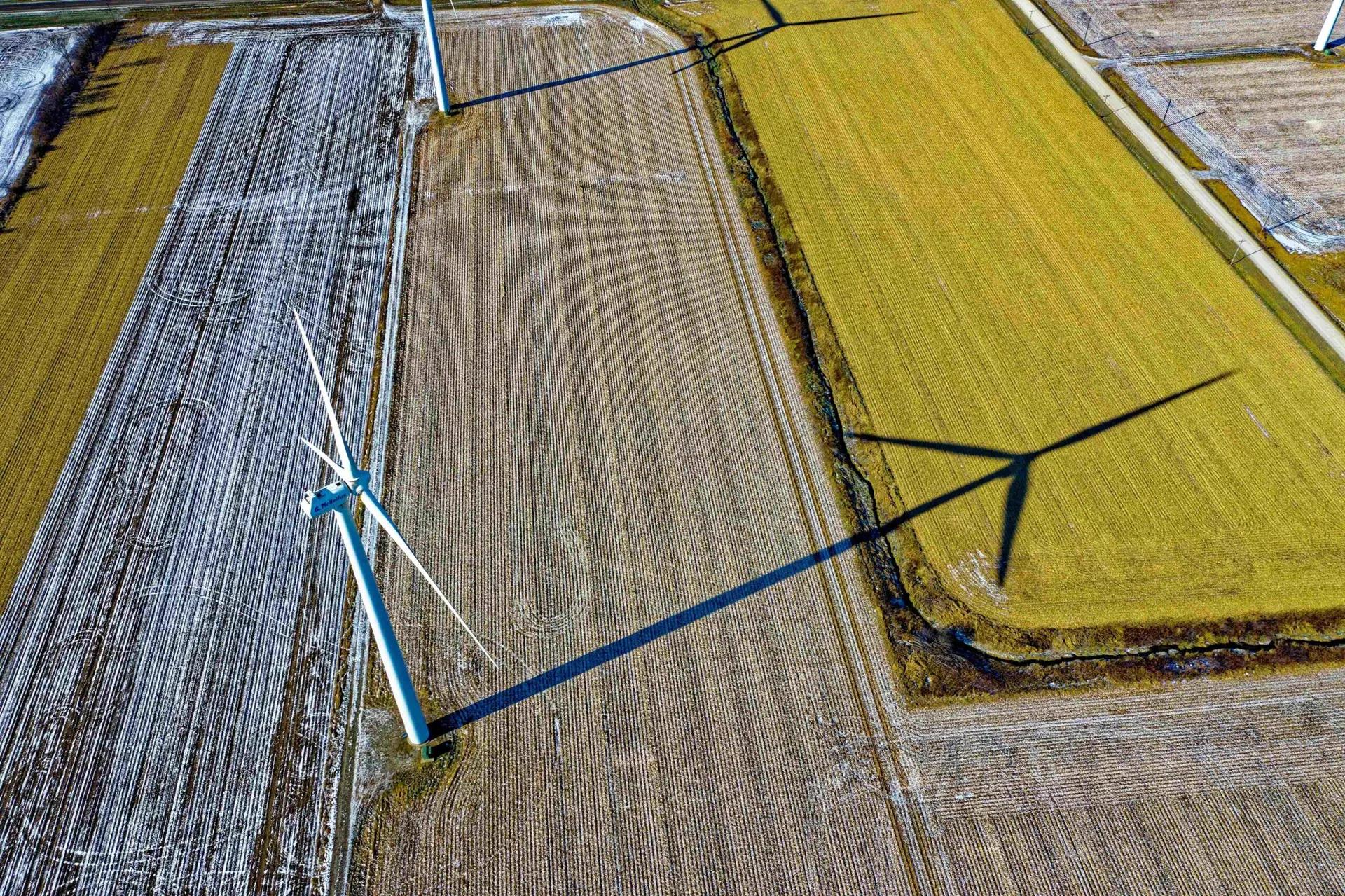 Descarbonização e parcerias entre empresas e ICTs para inovação Vista aérea de turbinas eólicas em campo agrícola com sombras longas projetadas no solo. Foco em energia limpa e sustentável.