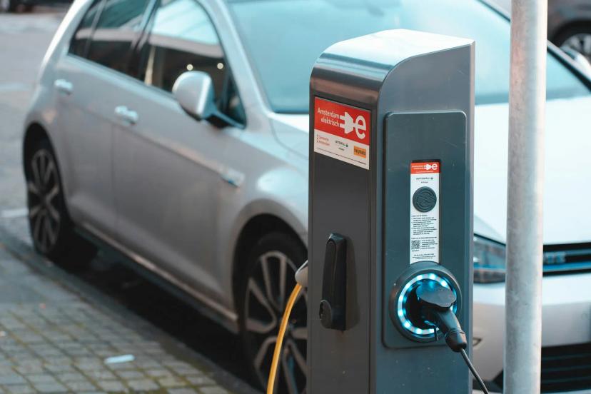 Carregamento de veículos elétricos e as novas tecnologias do setor Totem de carregamento de veículos elétricos com luz azul conectado a um carro prata estacionado na rua em Amsterdã.