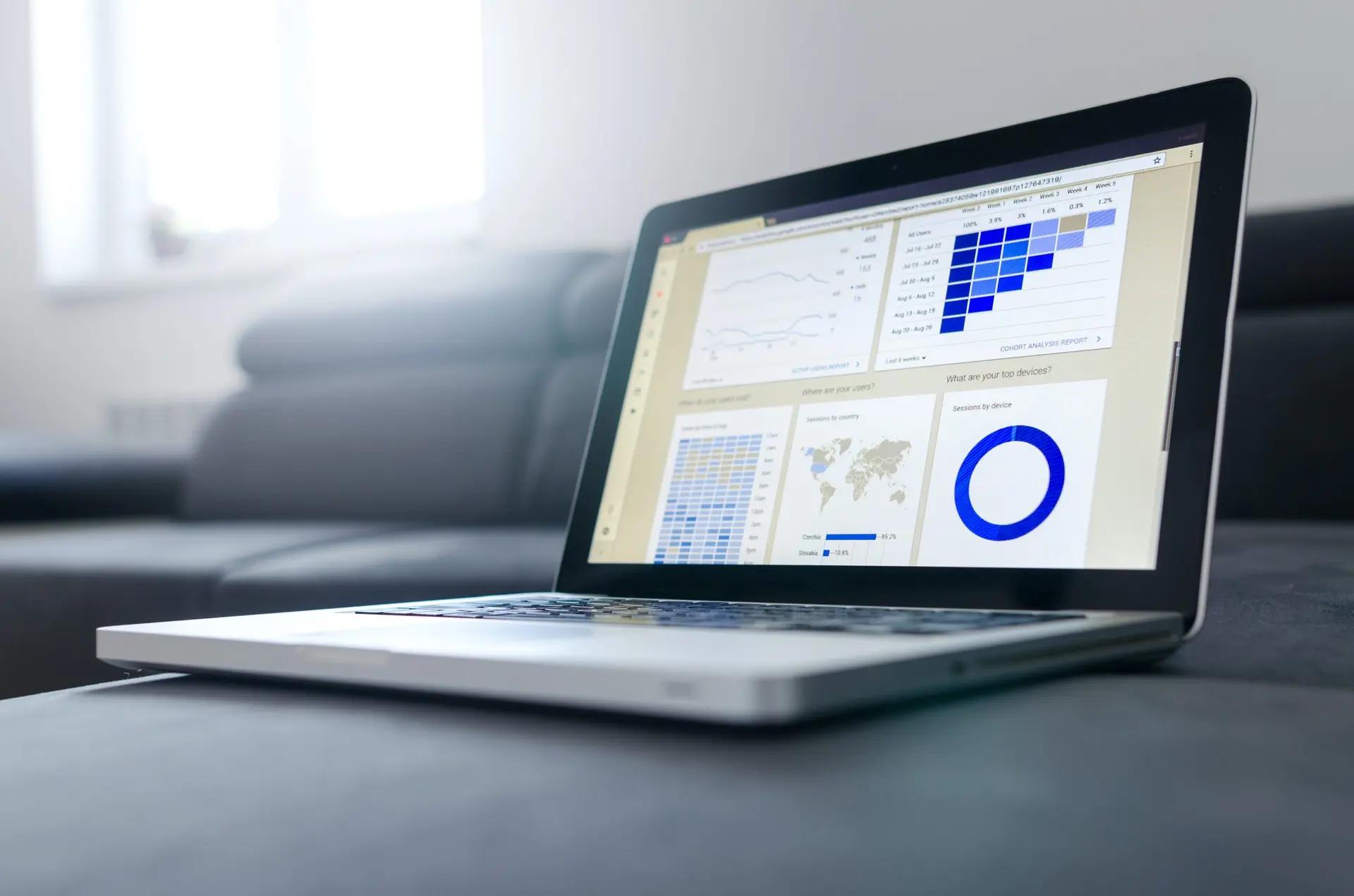 Sistemas legados e os desafios para a modernização data driven Laptop aberto sobre superfície cinza exibindo dashboard com gráficos de coorte, mapas e dados estatísticos coloridos em azul.