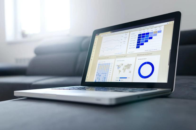 Sistemas legados e os desafios para a modernização data driven Laptop aberto sobre superfície cinza exibindo dashboard com gráficos de coorte, mapas e dados estatísticos coloridos em azul.