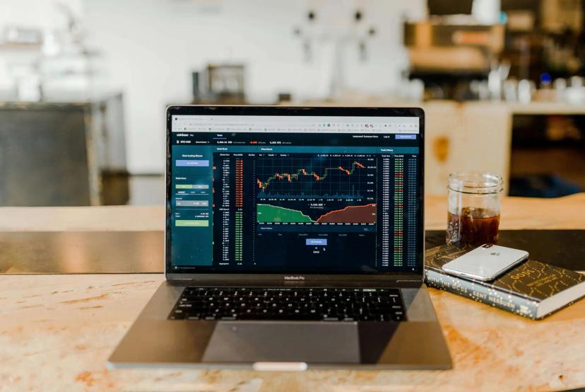Big Data ajuda o setor financeiro a ser mais data driven Laptop exibindo plataforma de negociação financeira com gráficos de velas e dados de mercado sobre mesa de madeira.
