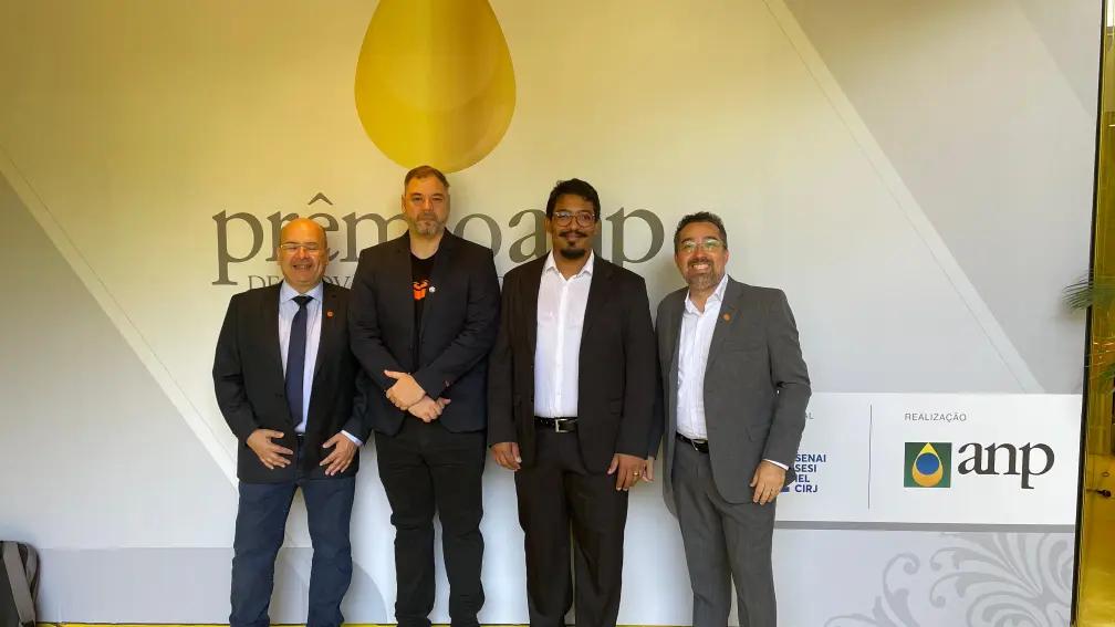 Quatro homens em trajes profissionais posam para foto em evento da Prêmio Petrobras de Inovação, com logo da ANP. Educação tecnológica, inovação, energia.