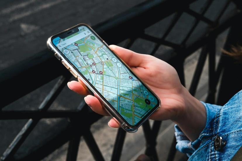 Mobilidade como serviço e inovação para o transporte sustentável Mão segura smartphone exibindo um mapa digital de rotas urbanas; pessoa usa jaqueta jeans em ambiente externo com grade ao fundo.
